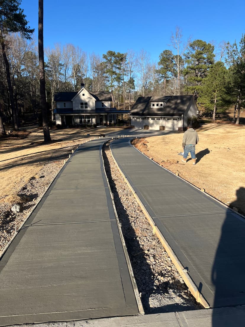 Concrete walkway leading to a house with trees in the background on a sunny day.