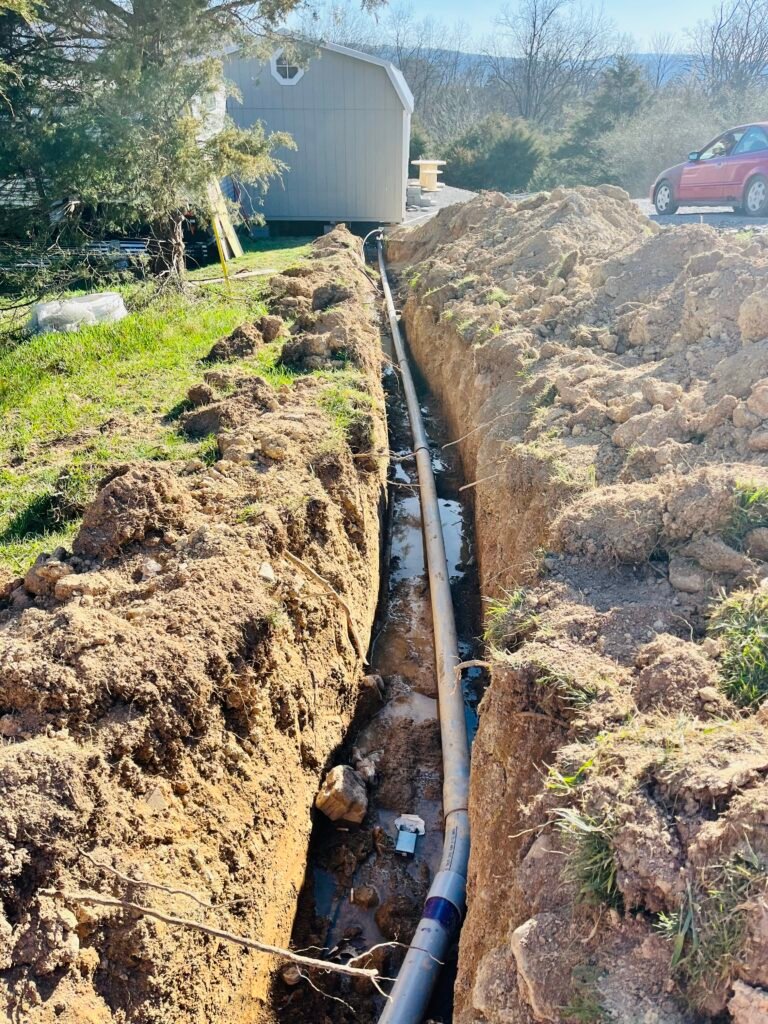 A sizable pipe lies on the ground amidst a wide, open field, surrounded by green grass and distant trees.
