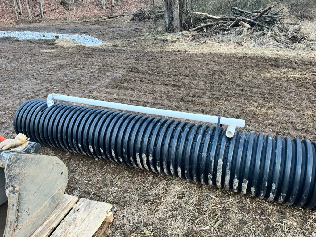 A large pipe rests on the ground in the center of a grassy field under a clear blue sky.
