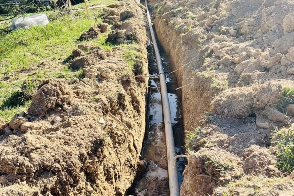Erosion-Control1-Risen-Sons A sizable pipe lies on the ground amidst a wide, open field, surrounded by green grass and distant trees.